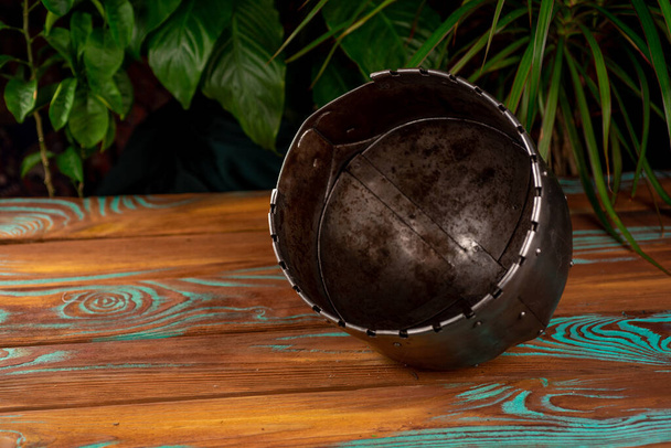inside view old metal reconstruction helmet with nose protection on wooden background with plants - Photo, image