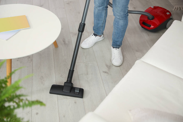Young man using vacuum cleaner at home, closeup - Foto, afbeelding