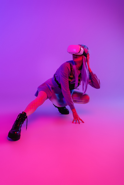 full length of woman in virtual reality headset sitting on purple and pink - Zdjęcie, obraz