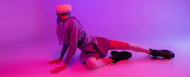 full length of young woman in virtual reality headset lying on purple background, banner - Valokuva, kuva