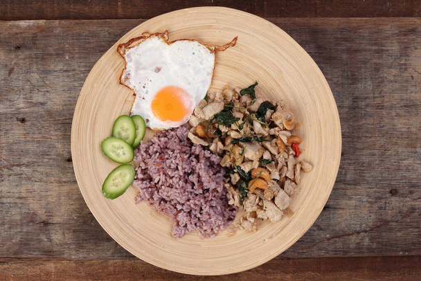 Tayland usulü kızarmış tavukla Tayland fesleğeni ve sade pirinç soslu yumurta soslu kaju fıstığı odunsu ahşap arka planda salatalık. - Fotoğraf, Görsel