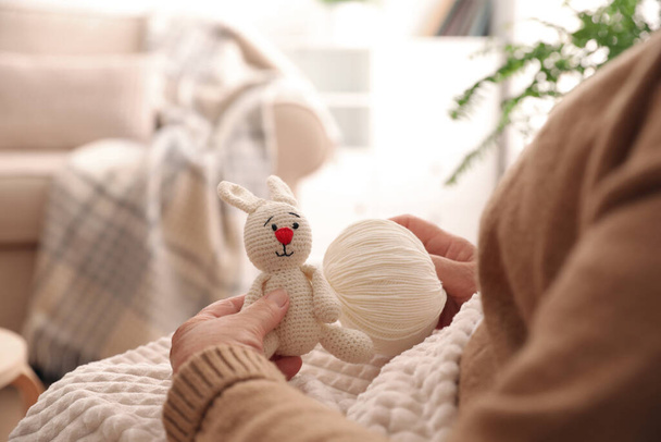 Elderly woman with knitted bunny at home, closeup. Creative hobby - 写真・画像