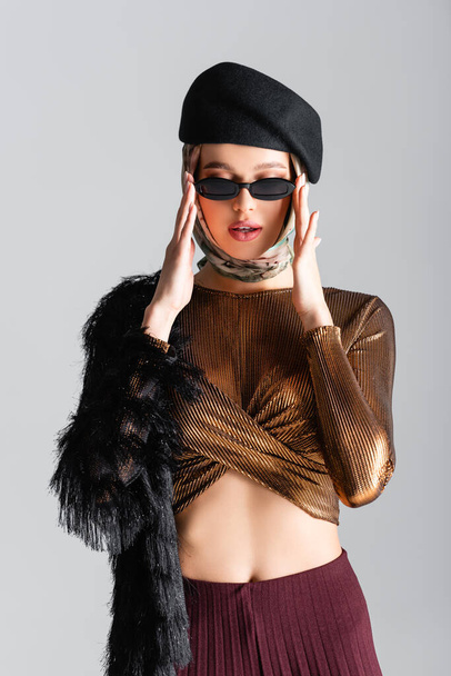 stylish woman in beret adjusting sunglasses isolated on grey - Fotografie, Obrázek