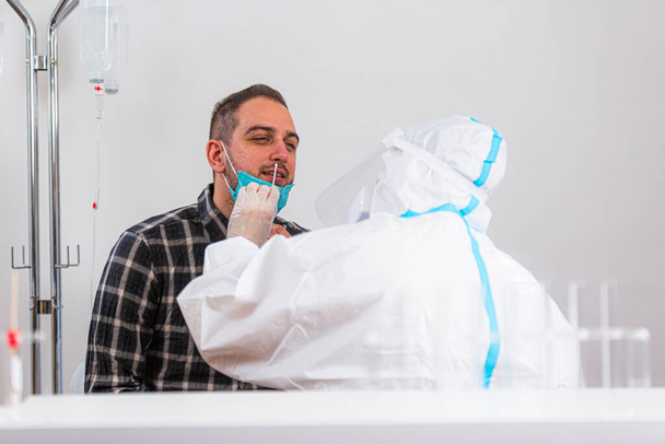Medische medewerker die de COVID-19 test uitvoert, neemt een neusmonster van een mannelijke patiënt in het ziekenhuislab, PCR-diagnose voor het Coronavirus, arts in PPE met behulp van testkit. - Foto, afbeelding