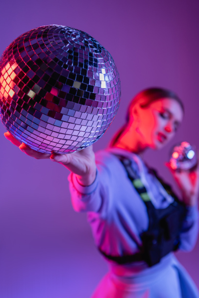 party disco ball in hand of trendy woman on purple and blurred background - 写真・画像