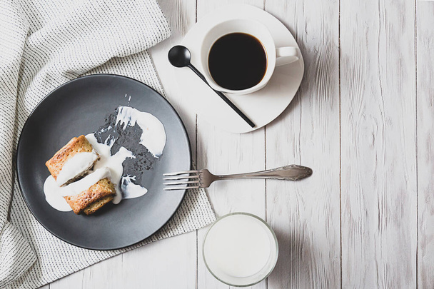 Pancakes with filling and sour cream, a glass of milk and a cup of black coffee on a light table. Rustic breakfast with copy space top view - Photo, Image