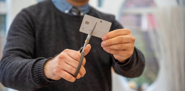 man holding credit card cut into halves and looking happy debt payout. cutting credit card. Man cutting debit card scissors Hands of man cutting a credit card with scissors. financial problems at home - Φωτογραφία, εικόνα