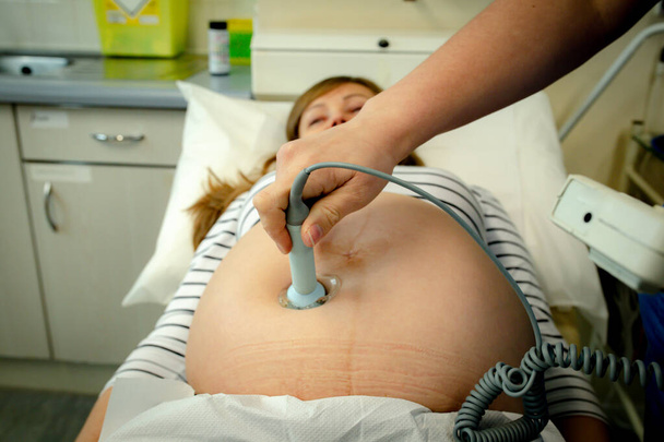 Vroedvrouw onderzoekt buik van zwangere vrouw met CTG-scan. Zwangere vrouw wordt onderzocht door verpleegster verloskundige vroedvrouw met behulp van doppler monitor. Arts het uitvoeren van een echo scan op zwangere vrouw - Foto, afbeelding