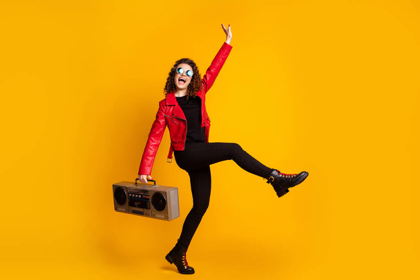 Фотографія повної довжини божевільної дівчини, що тримає бум-коробку, піднімає шкіряні штани, ізольовані на блискучому кольоровому фоні
 - Фото, зображення