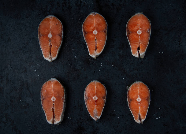 Pattern of salmon steaks laid out in rows, on a dark black and blue background, top view. - Zdjęcie, obraz