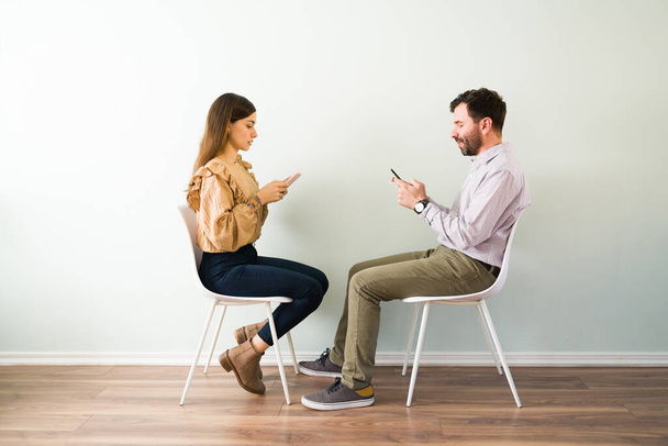 Side view of a attractive couple that met trough an internet dating site are texting and flirting with each other on their smartphone  - Foto, imagen