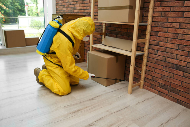 Pest control worker in protective suit spraying pesticide indoors - Fotó, kép