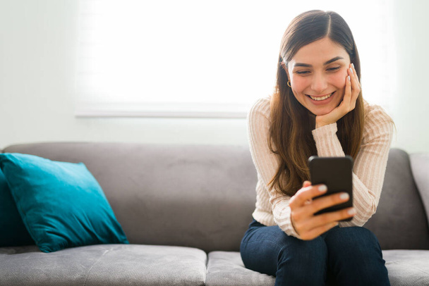 Mulher jovem hispânica em um relacionamento é feliz e sorrindo ao ler as mensagens de texto amorosas de seu namorado  - Foto, Imagem