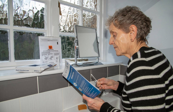 England, UK. 2021. Woman in bathroom studying the instructions of a Coronavirus, Covid-19 Home Test kit  - Fotó, kép