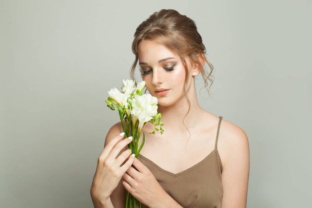Υγιής νεαρή γυναίκα που κρατά λευκά λουλούδια σε λευκό φόντο - Φωτογραφία, εικόνα