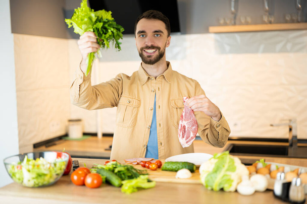 Nice guy with pretty smile is showing that he prefers vegetables to meat to save animals. He looks healthy and happy being vegetarian - 写真・画像
