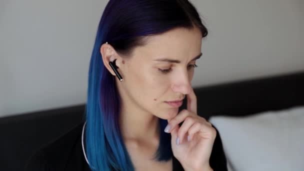 Bedachtzame jonge vrouw die op het bed zit en een draadloze hoofdtelefoon draagt - Video