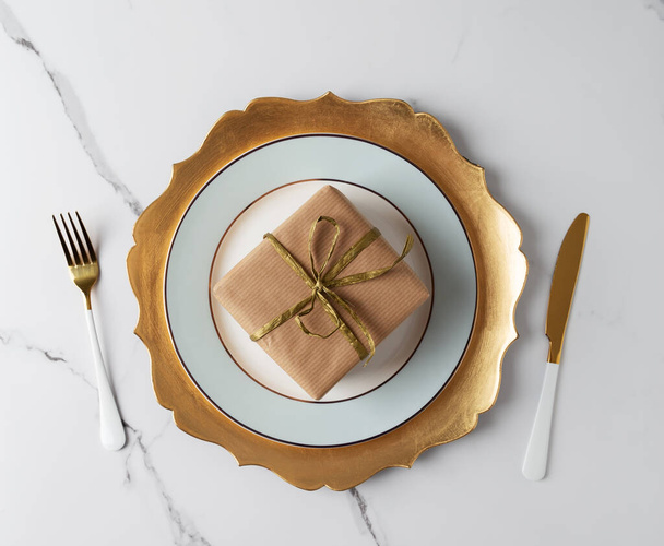 Festive table set with gold tableware and gift box at white marble table. Top view, flat lay, concept of holiday table set - 写真・画像