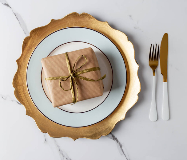 Festive table set with gold tableware and gift box at white marble table. Top view, flat lay, concept of holiday table set - 写真・画像