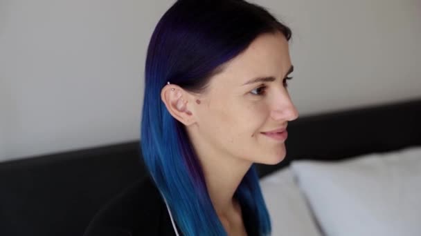 Νεαρή χαρούμενη γυναίκα με μπλε μαλλιά βάζει ασύρματα ακουστικά - Πλάνα, βίντεο