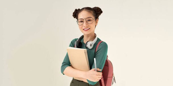 Joven estudiante feliz lleva cuaderno y pluma sobre fondo blanco  - Foto, Imagen