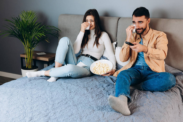 Sweet couple has quarantine free time watch movie impressed surprised unexpected thriller film ending covering her eyes with pop corn box sit sofa in house indoors. Lovely couple watching tv show and - Photo, Image