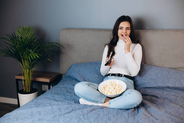 Pretty woman is smiling . Pretty female has quarantine free time watch movie impressed surprised unexpected film movie ending hold big pop corn box sit sofa in house indoors. - Fotografie, Obrázek