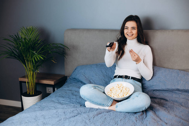 Nice woman is smiling . Pretty female has quarantine free time watch movie impressed surprised unexpected film movie ending hold big pop corn box sit sofa in house indoors. - Photo, Image