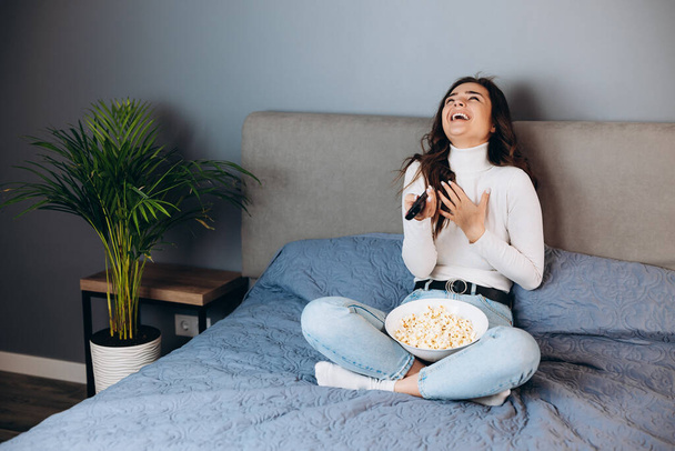 Nice woman is laughing . Pretty female has quarantine free time watch movie impressed surprised unexpected film movie ending hold big pop corn box sit sofa in house indoors. - Foto, Imagen