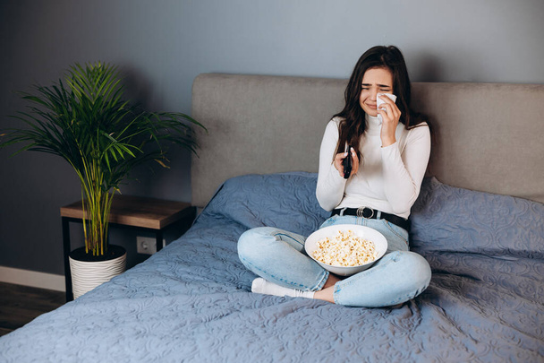 Sweet woman is crying. Pretty female has quarantine free time watch movie impressed surprised unexpected film movie ending hold big pop corn box sit sofa in house indoors. - Photo, Image