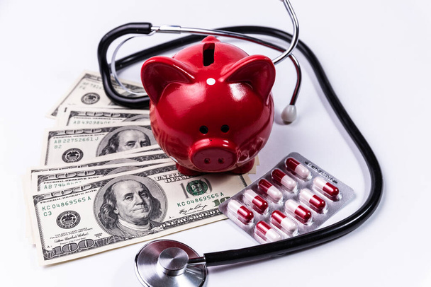 Piggy bank, tablets, stethoscope resting on pile of dollars on white background - Photo, image