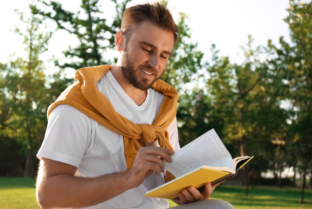Young man reading book in park on sunny day - Photo, Image