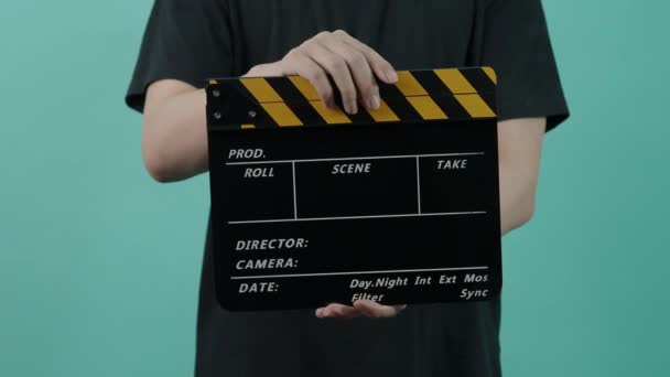 Film Clapperboard. L'équipe de tournage tient la main et applaudit l'ardoise de film à rayures noires et jaunes vide dans le cadre. 3 2 1 Action. clapperboard de couleur jaune et noire sur fond bleu vert. Production vidéo - Séquence, vidéo