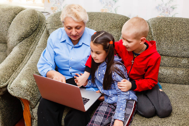 Бабуся з онуками використовує ноутбук вдома
 - Фото, зображення
