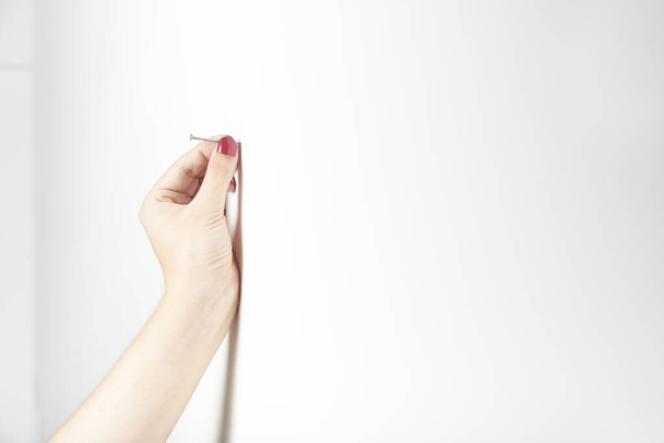 Manicura de la mano de una joven mujer sosteniendo un clavo en la pared, para martillarlo. Imagen brillante con espacio de copia. - Foto, Imagen