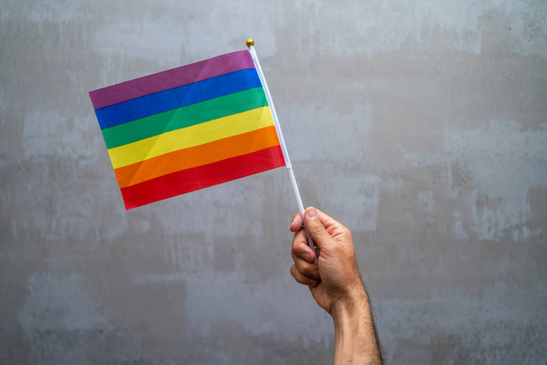 Человек держит за руку и размахивает флагом ЛГБТ-гордости. Многоцветное движение радужного флага мира. Оригинальный красочный символ гей-гордости - Фото, изображение