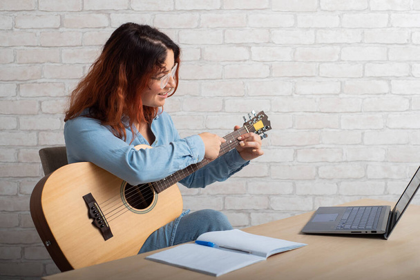 Caucasian woman remotely teaches guitar playing on laptop. Online music training - Fotó, kép