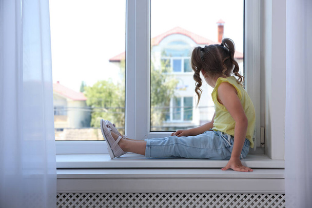 Cute little girl on window sill at home - Foto, imagen