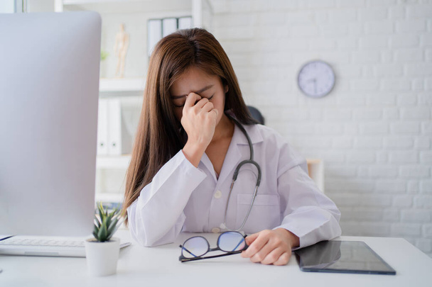 Asiatische Ärztin ruht sich im Untersuchungsraum aus Sie spürt Kopfschmerzen und Stress. - Foto, Bild