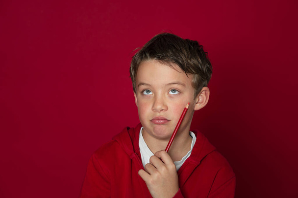 cool young school boy is posing with red pencil in ront of red background - Foto, imagen