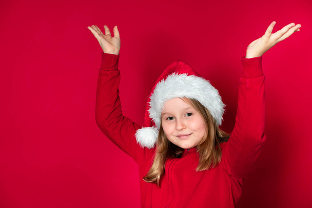 girl with Santa Claus hat and red sweater in front of red background - Foto, Bild