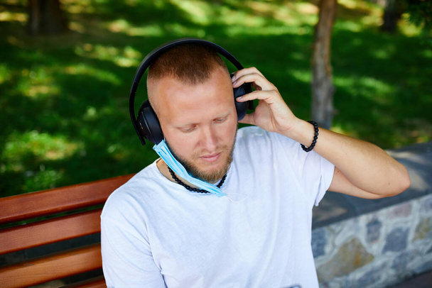 Man die muziek luistert met hoofdtelefoon, gezichtsbeschermend masker buiten in het park draagt, levensstijl nieuw normaal, Quarantaine, coronavirus. - Foto, afbeelding