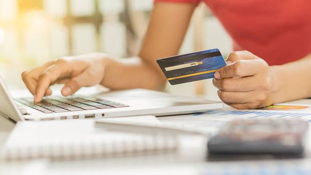 Hand hält eine blaue Kreditkarte in der Hand und benutzt einen Laptop, um online einzukaufen und die Nummer auf der Kreditkarte zu wählen. - Foto, Bild