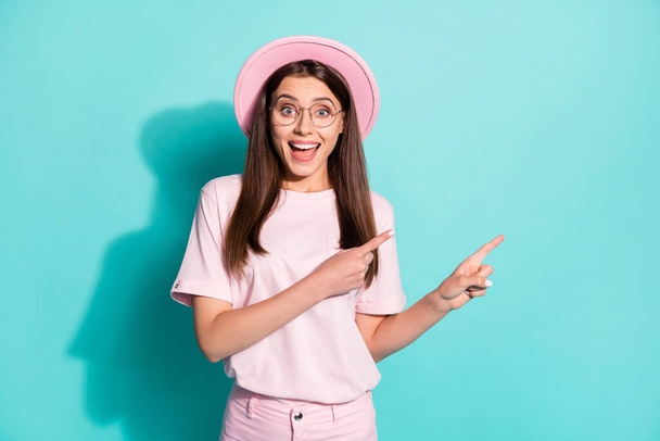 Photo of cute surprised student girl dressed pink t-shirt headwear pointing two fingers empty space open mouth isolated turquoise color background - Foto, Imagen