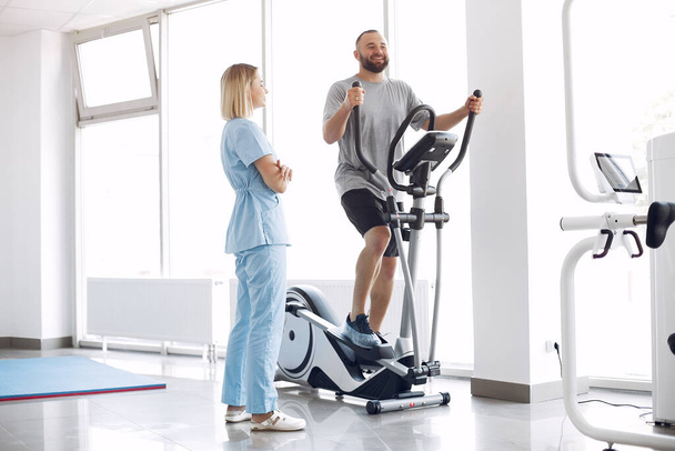 Пацієнт виконує вправи на спін-велосипеді в спортзалі з терапевтом
 - Фото, зображення
