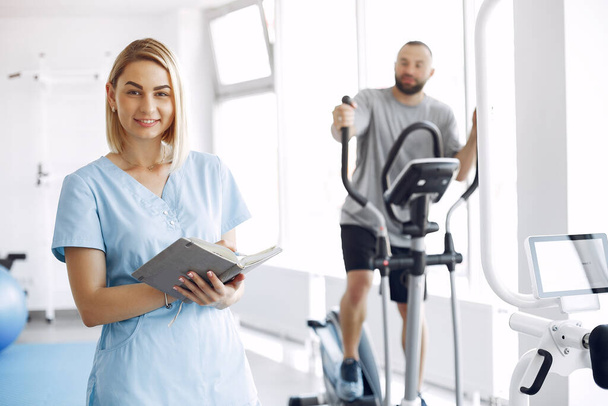 Patient doing exercise on spin bike in gym with therapist - Foto, Bild