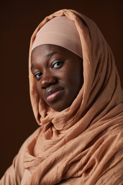 Vertical portrait of ethnic African-American woman wearing headscarf and looking at camera while posing in studio - Photo, Image