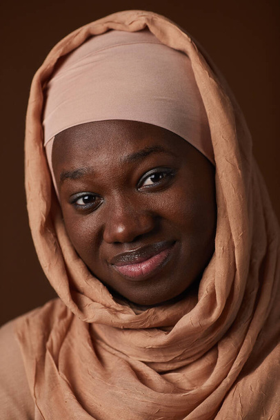 Κάθετη κοντινή φωτογραφία μιας Αφρο-Αμερικανίδας που φοράει μαντίλα και χαμογελάει στην κάμερα ενώ ποζάρει στο στούντιο - Φωτογραφία, εικόνα