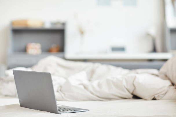 Image de fond minimale d'un ordinateur portable mince sur un lit confortable avec des draps en coton blanc à l'intérieur de la maison, espace de copie - Photo, image