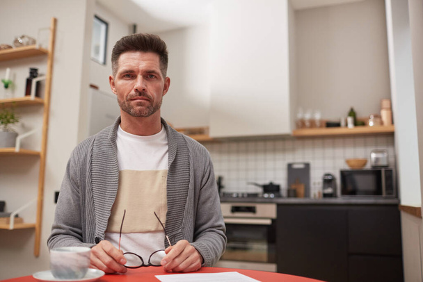 Портрет красивого зрілого чоловіка, який дивиться на камеру, сидячи за столом в інтер'єрі кухні, копіює простір
 - Фото, зображення